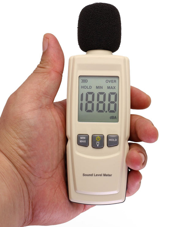 Hand holding a sound level meter with digital display on a white background