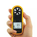 Hand holding a yellow anemometer with digital display on a white background